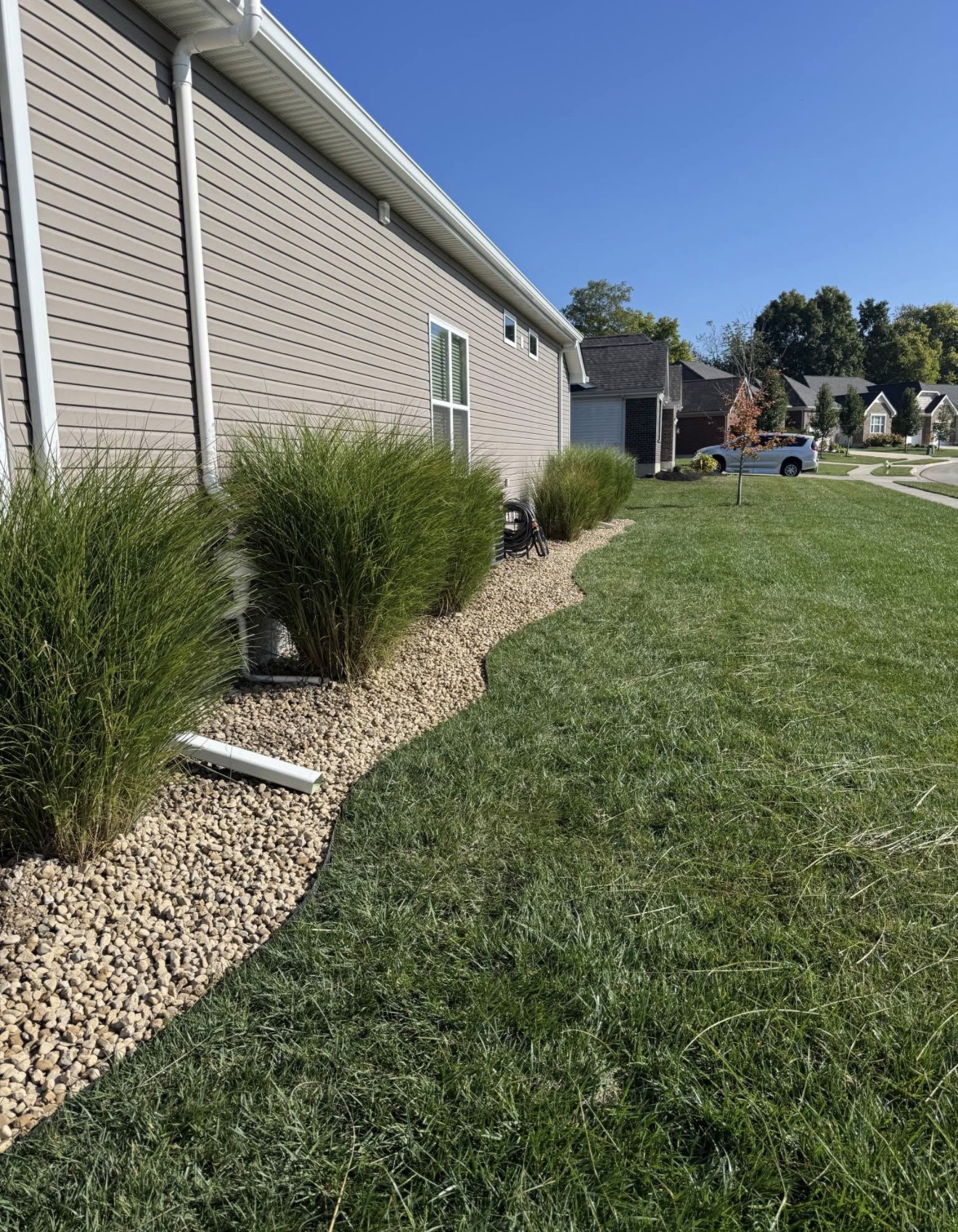 A curved stone landscape bed with ornamental grasses beside a home